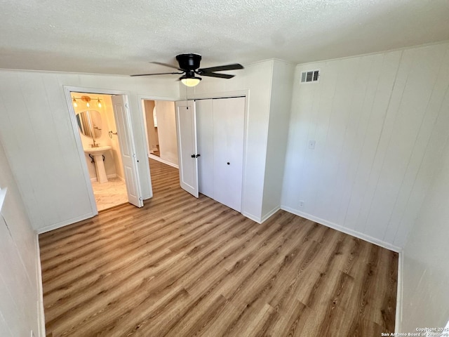 unfurnished bedroom with ceiling fan, ensuite bathroom, a textured ceiling, a closet, and light wood-type flooring