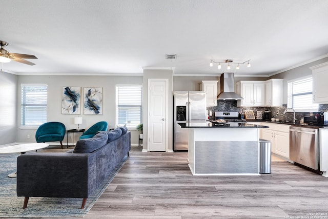 kitchen featuring stainless steel appliances, white cabinetry, ornamental molding, and wall chimney range hood