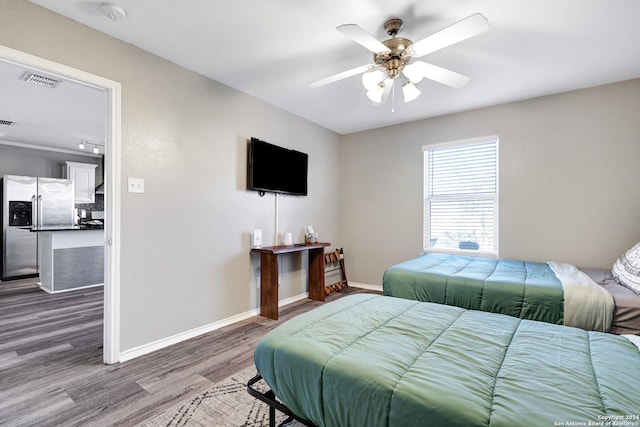 bedroom with hardwood / wood-style flooring, ceiling fan, and stainless steel refrigerator with ice dispenser