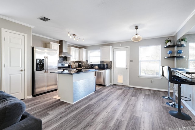 kitchen featuring white cabinetry, wall chimney range hood, pendant lighting, appliances with stainless steel finishes, and light wood-type flooring