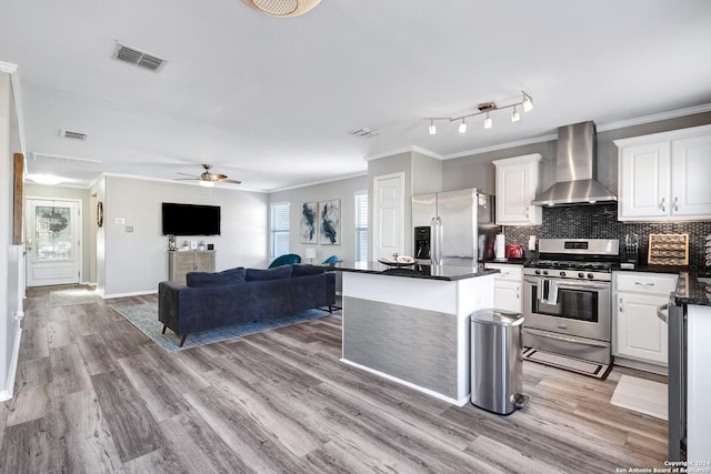 kitchen featuring white cabinetry, stainless steel appliances, wall chimney range hood, light hardwood / wood-style flooring, and backsplash