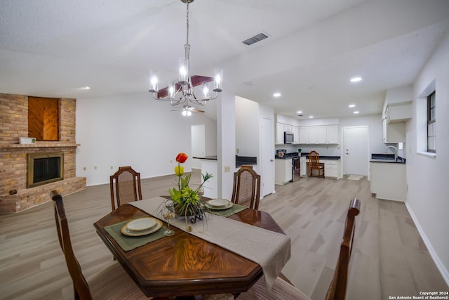 dining area featuring a brick fireplace, light hardwood / wood-style floors, sink, and a chandelier