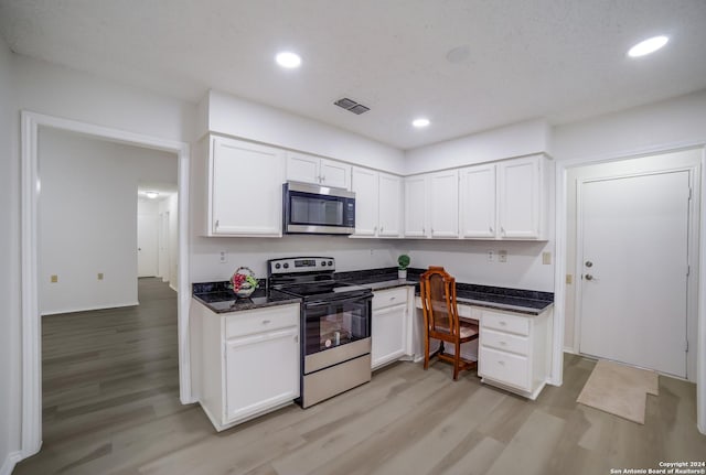 kitchen featuring dark stone counters, white cabinets, built in desk, light wood-type flooring, and appliances with stainless steel finishes