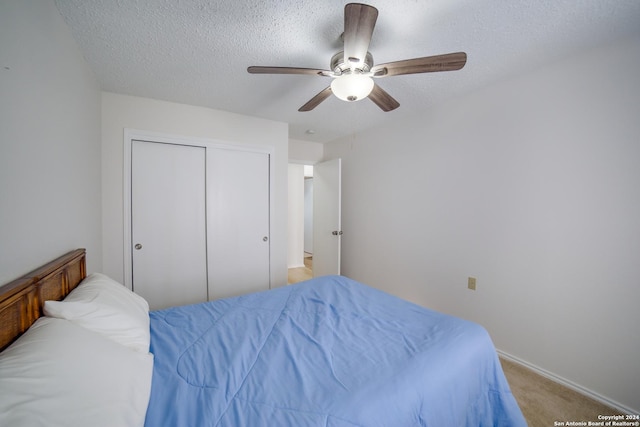 bedroom featuring ceiling fan, a closet, light colored carpet, and a textured ceiling