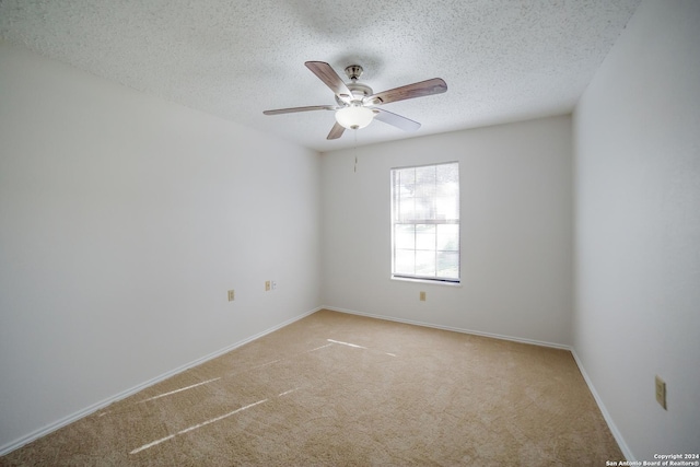 empty room with ceiling fan, light colored carpet, and a textured ceiling