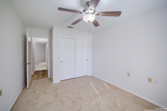 unfurnished bedroom featuring ceiling fan, a closet, light carpet, and a textured ceiling