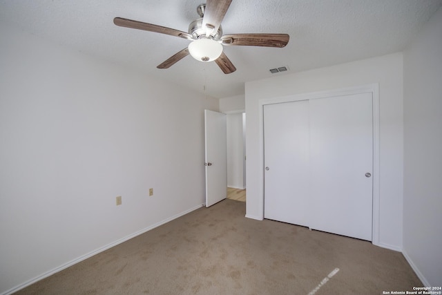 unfurnished bedroom with ceiling fan, a closet, light colored carpet, and a textured ceiling