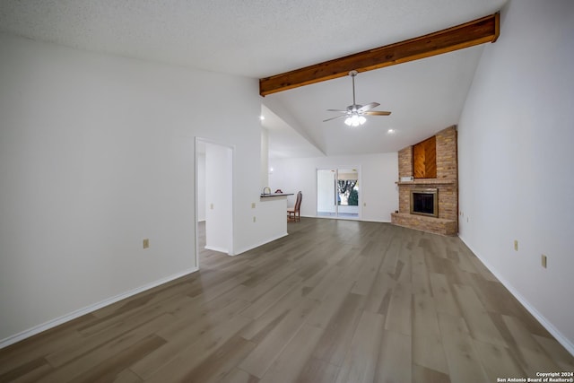 unfurnished living room with vaulted ceiling with beams, ceiling fan, a textured ceiling, and a brick fireplace