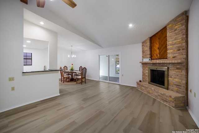 living room with ceiling fan with notable chandelier, vaulted ceiling, sink, a fireplace, and light hardwood / wood-style floors