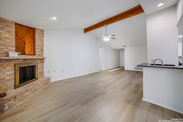 unfurnished living room with ceiling fan, sink, a brick fireplace, lofted ceiling with beams, and light wood-type flooring