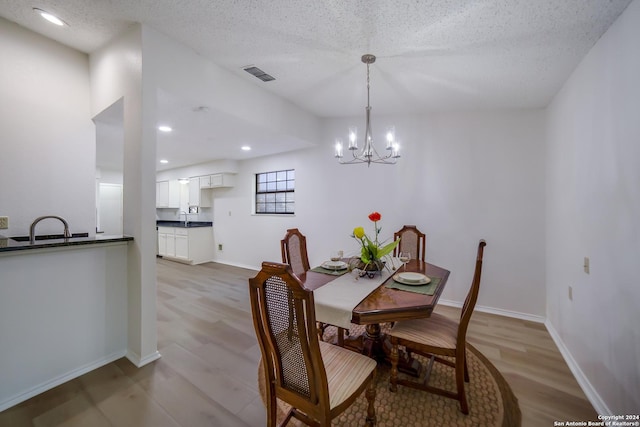 dining room with a notable chandelier, a textured ceiling, and light hardwood / wood-style flooring