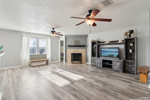 unfurnished living room featuring a textured ceiling, light wood-type flooring, ceiling fan, and a tiled fireplace