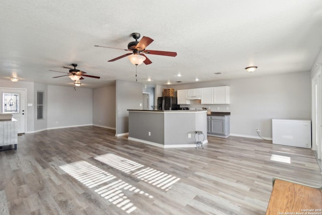 unfurnished living room featuring ceiling fan, a textured ceiling, and light hardwood / wood-style flooring