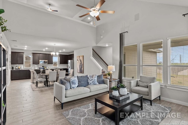 living room with ceiling fan with notable chandelier and high vaulted ceiling