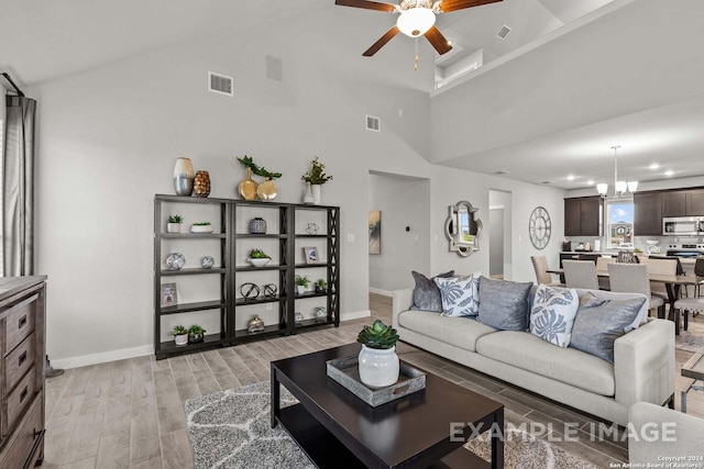 living room with ceiling fan with notable chandelier, light wood-type flooring, and a towering ceiling