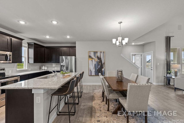 kitchen with a kitchen island with sink, sink, decorative light fixtures, dark brown cabinetry, and stainless steel appliances