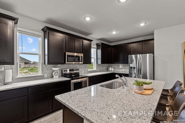 kitchen with a center island with sink, a kitchen breakfast bar, sink, light stone counters, and stainless steel appliances