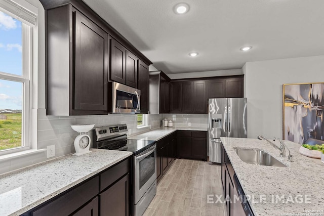 kitchen featuring backsplash, light stone counters, dark brown cabinets, stainless steel appliances, and sink