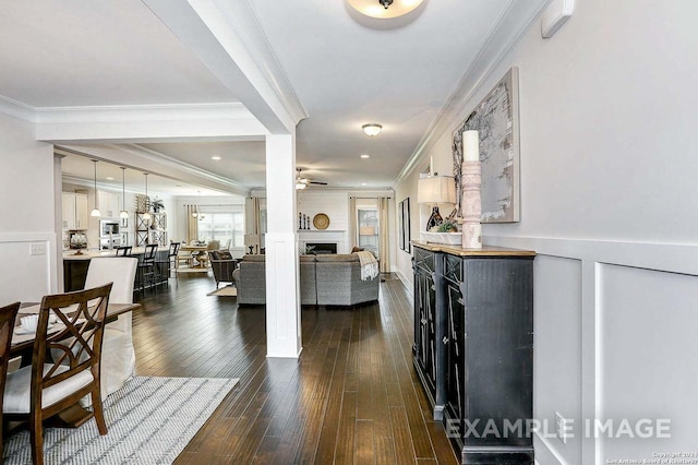 interior space with ceiling fan, a large fireplace, dark hardwood / wood-style flooring, and crown molding