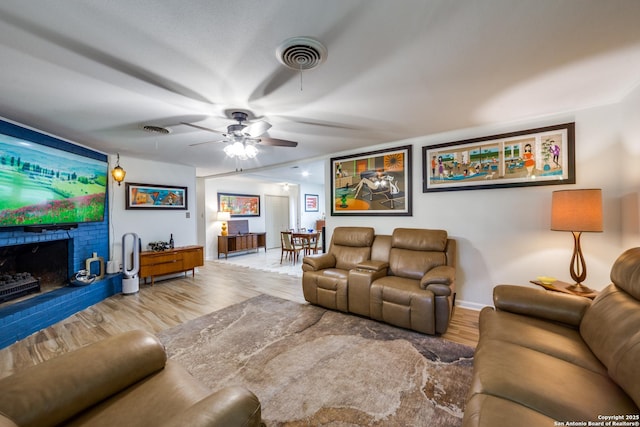 living room featuring ceiling fan, wood-type flooring, and a brick fireplace