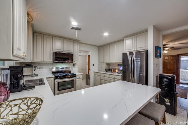 kitchen featuring a breakfast bar, backsplash, white cabinets, appliances with stainless steel finishes, and kitchen peninsula