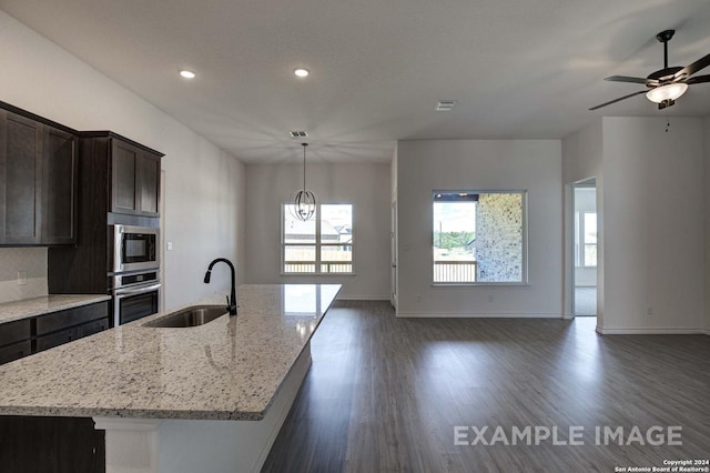 kitchen featuring light stone countertops, stainless steel appliances, a center island with sink, and sink