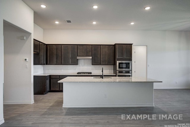 kitchen with backsplash, sink, light stone countertops, an island with sink, and appliances with stainless steel finishes