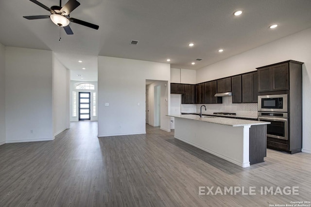 kitchen featuring light wood-type flooring, stainless steel appliances, a center island with sink, and backsplash