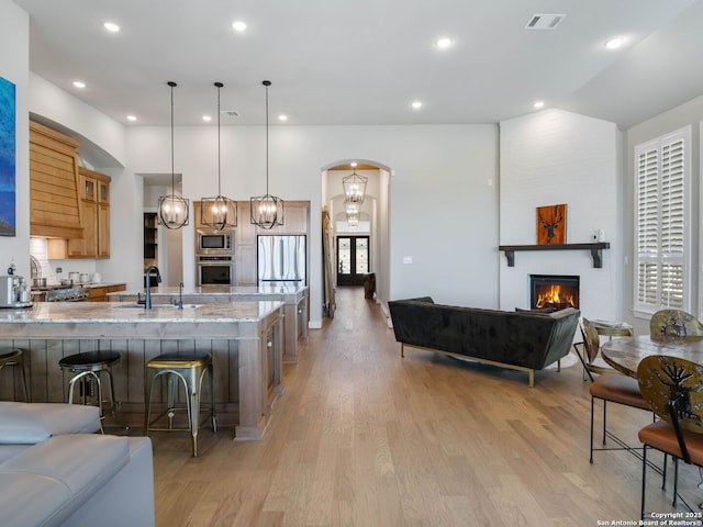 kitchen with appliances with stainless steel finishes, light stone countertops, pendant lighting, a breakfast bar, and sink