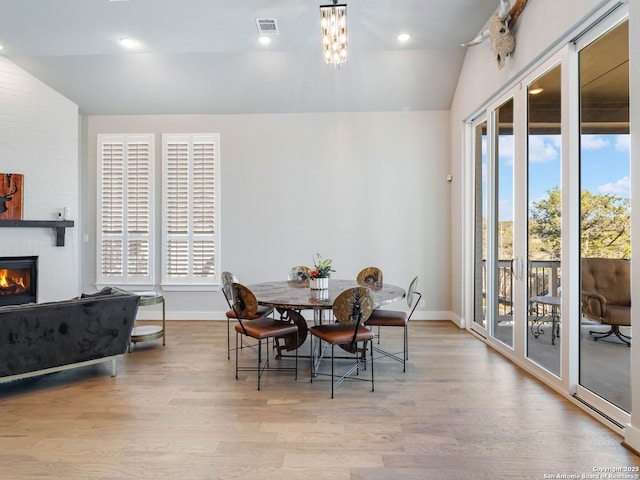 dining space with a fireplace, vaulted ceiling, and light hardwood / wood-style floors