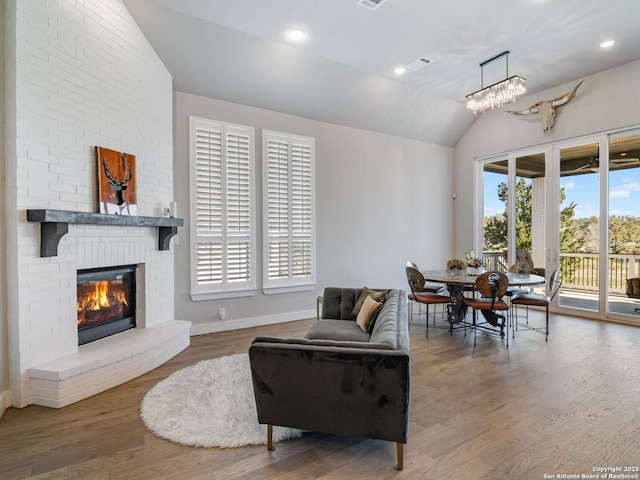 living room featuring wood-type flooring, a brick fireplace, and vaulted ceiling