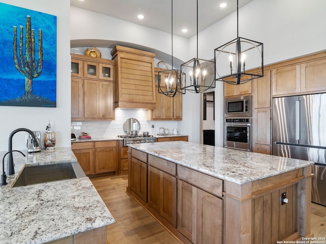 kitchen with stainless steel appliances, pendant lighting, light stone counters, a kitchen island, and sink