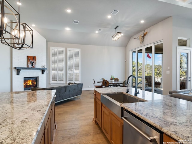 kitchen with light stone counters, stainless steel dishwasher, hanging light fixtures, a brick fireplace, and sink