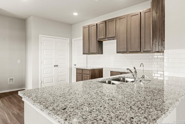 kitchen with light stone countertops, sink, dark hardwood / wood-style floors, kitchen peninsula, and decorative backsplash