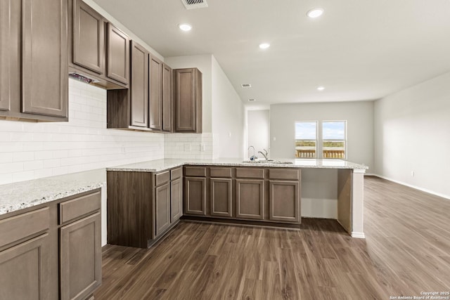 kitchen featuring kitchen peninsula, dark hardwood / wood-style flooring, tasteful backsplash, and light stone countertops