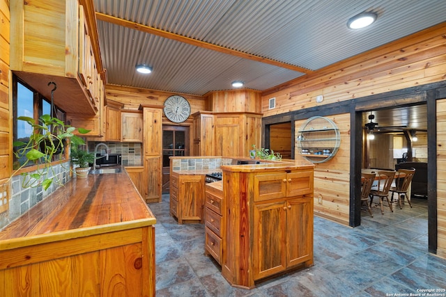 kitchen with wood counters, ceiling fan, sink, a kitchen island, and wood walls