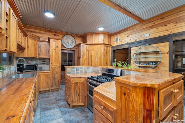 kitchen with wood counters, wood walls, sink, stainless steel gas range, and a kitchen island