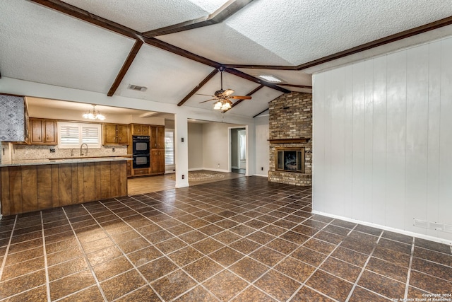 unfurnished living room featuring a fireplace, a textured ceiling, ceiling fan with notable chandelier, and lofted ceiling with beams