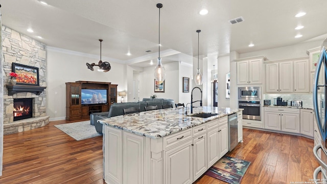 kitchen with sink, stainless steel appliances, light stone counters, a kitchen island with sink, and a fireplace