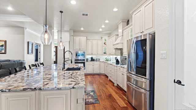 kitchen featuring a kitchen bar, appliances with stainless steel finishes, light stone countertops, a large island with sink, and pendant lighting