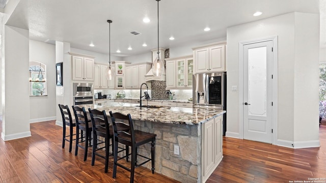 kitchen with a kitchen bar, light stone counters, stainless steel appliances, decorative light fixtures, and an island with sink