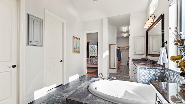 bathroom featuring vanity, vaulted ceiling, and tiled tub