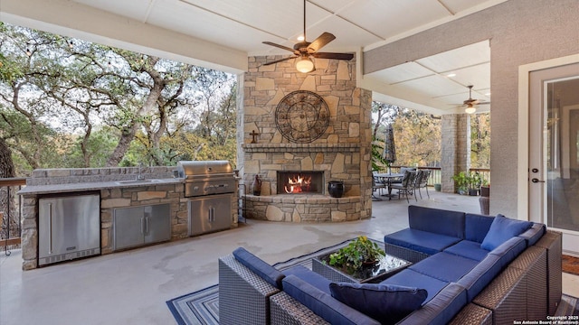 view of patio with an outdoor living space with a fireplace, sink, ceiling fan, a grill, and exterior kitchen