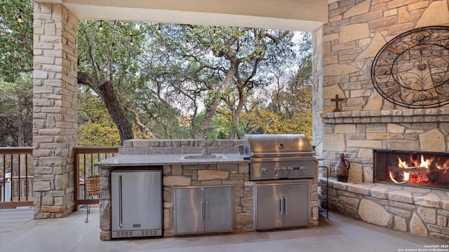 view of patio / terrace featuring sink, an outdoor stone fireplace, a grill, and exterior kitchen