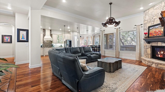 living room with a stone fireplace, ornamental molding, and dark wood-type flooring