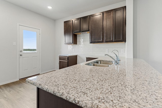 kitchen with backsplash, light stone counters, dark brown cabinetry, and sink