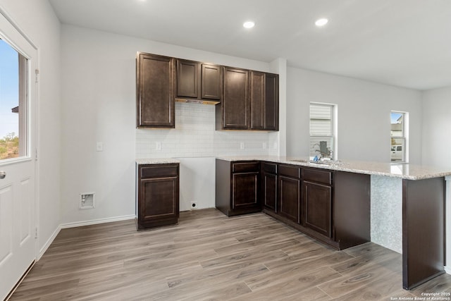 kitchen featuring kitchen peninsula, backsplash, dark brown cabinets, sink, and light hardwood / wood-style floors