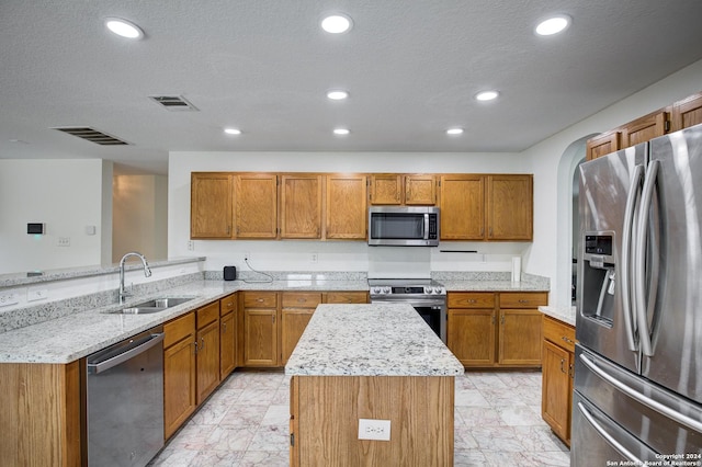 kitchen with kitchen peninsula, appliances with stainless steel finishes, light stone countertops, sink, and a center island