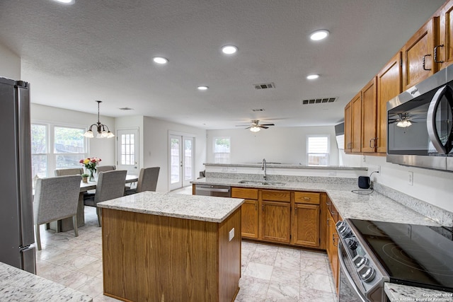 kitchen with sink, stainless steel appliances, kitchen peninsula, pendant lighting, and a kitchen island