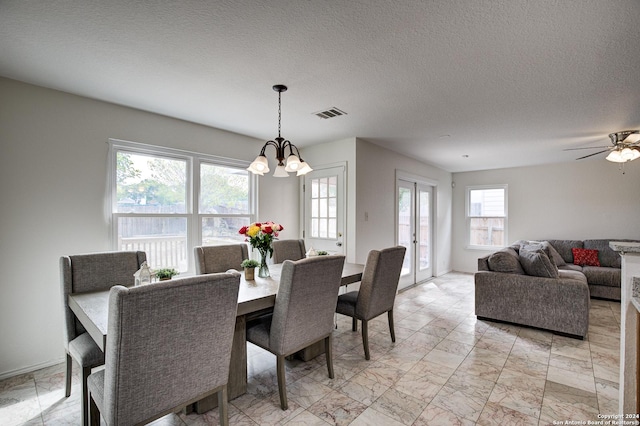 dining room with ceiling fan with notable chandelier and a textured ceiling